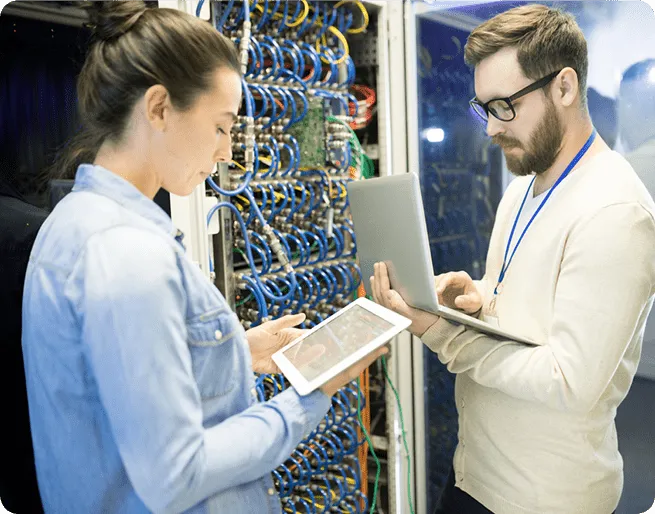 IT professionals reviewing data center server racks using a tablet and laptop